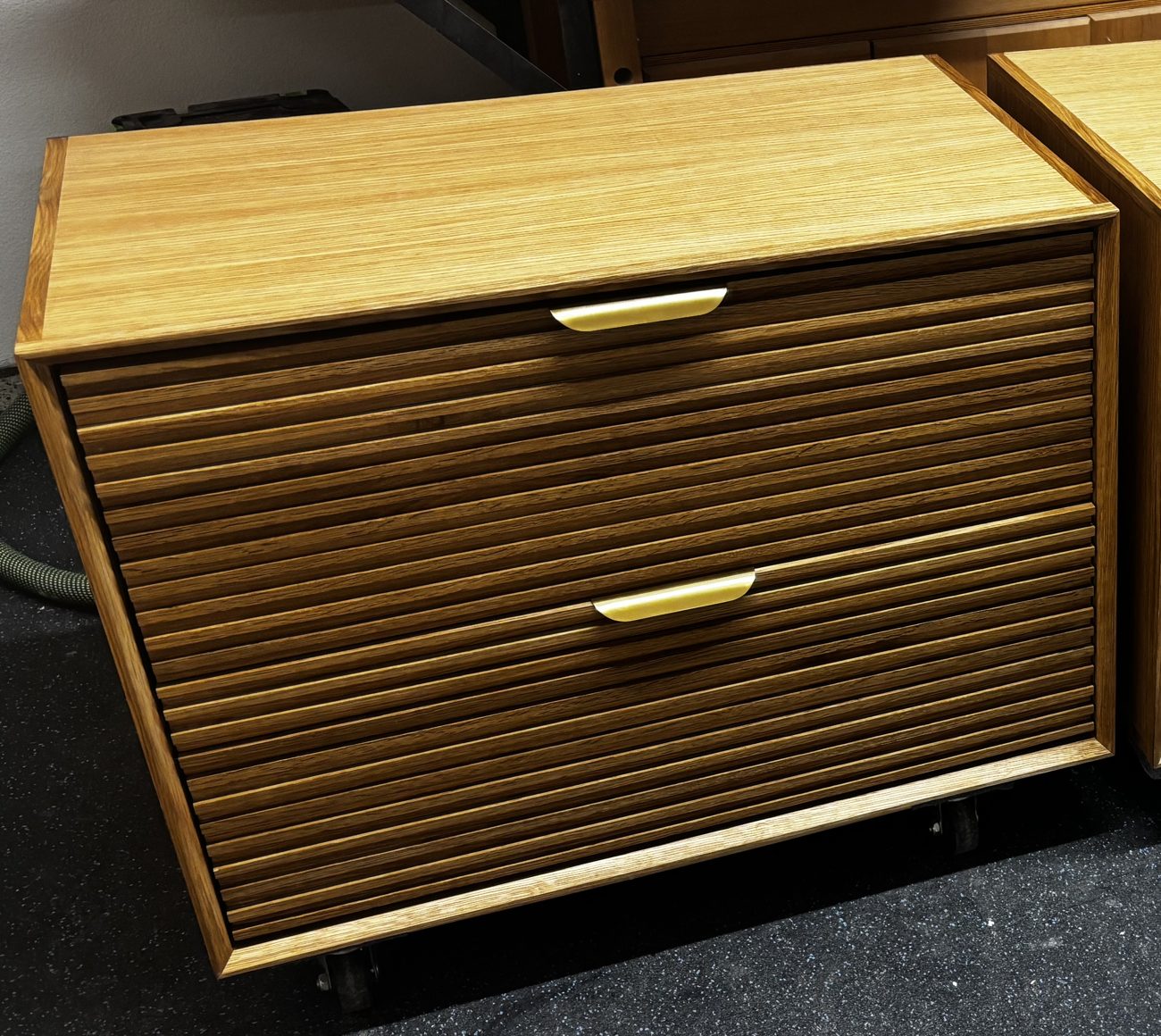 The finished white oak night stand with a horizontally slatted front and brass pulls